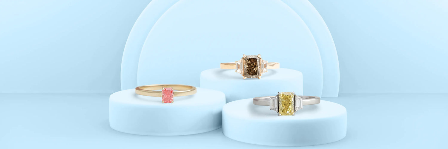 Three radiant cut lab-grown diamond engagement rings in yellow gold — three-stone with oval side stones, classic four-prong solitaire with plain band, and full bezel solitaire on tiered grey stone display