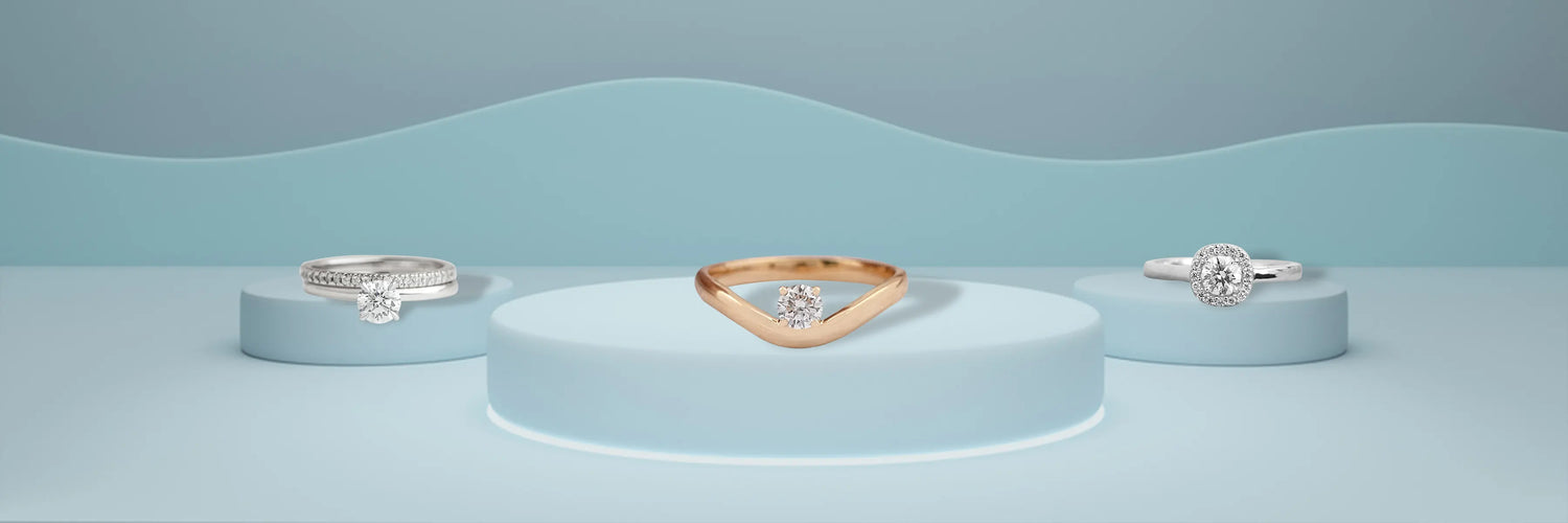 Three round cut lab-grown diamond engagement rings in white gold — bypass solitaire, six-prong classic solitaire, and round brilliant halo with pavé band on sandy beige surface